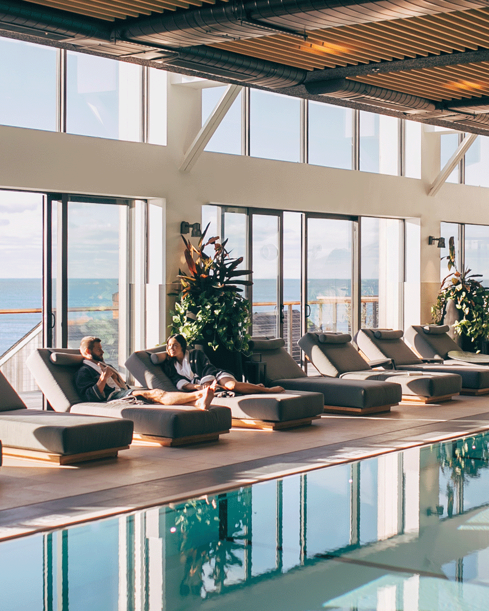 GIF showing couple lounging by indoor pool, waves crashing in front of pink skyline, shoreline view of 168极速赛车官方开奖结果记录体彩 Resort & 极速赛车168一分钟开奖记录体彩-开奖结果预测官网直播 seawater spa.