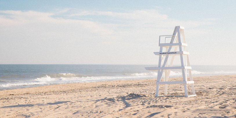 Sunny beach with a white lifeguard chair overlooking the calm ocean waves.