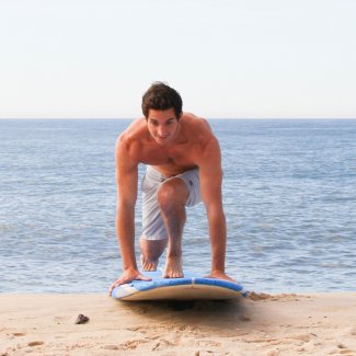 Man practicing balance on a surfboard at the beach, ocean in the background.