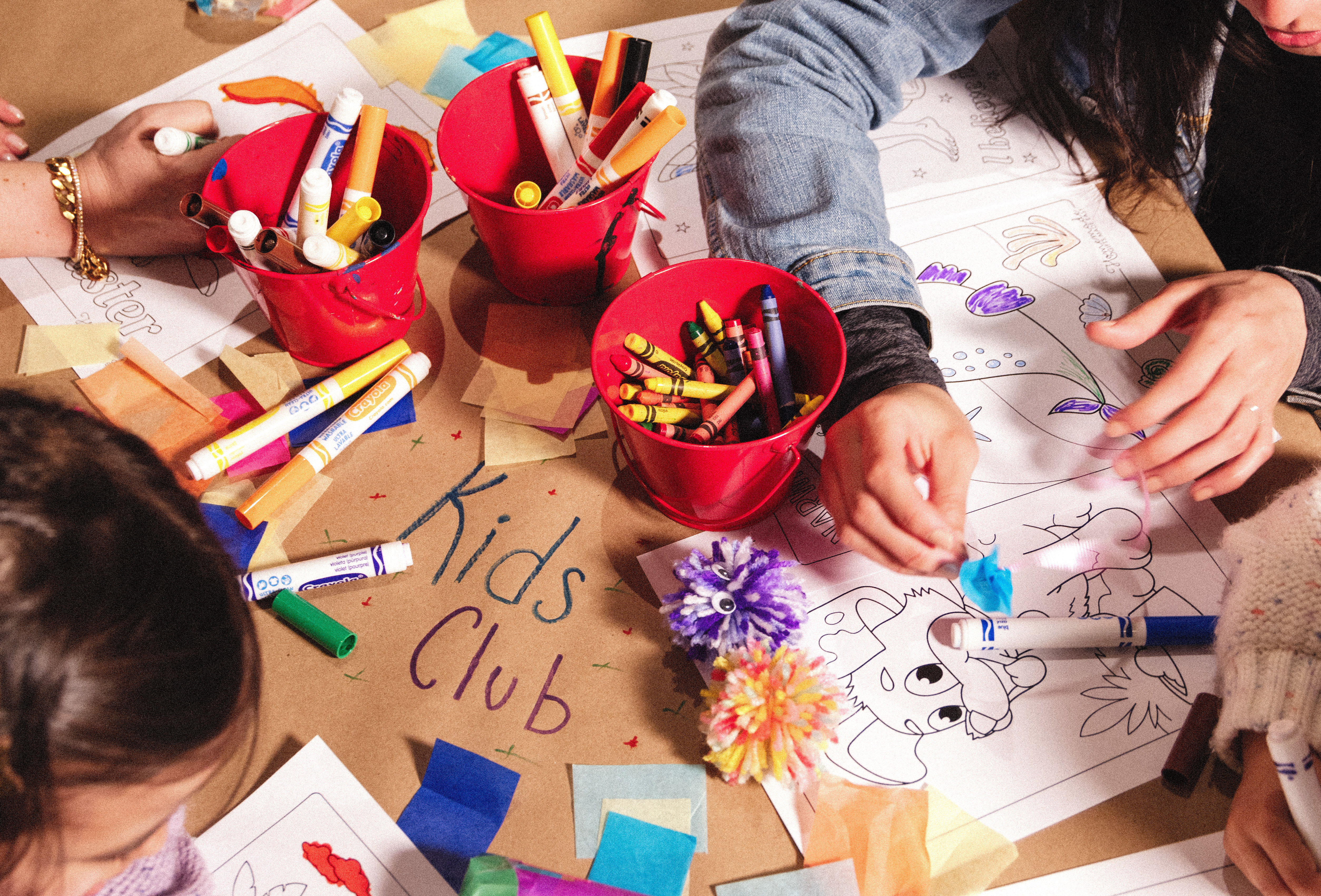 Close up of kid's hands working on art project with colorful paper and markers.
