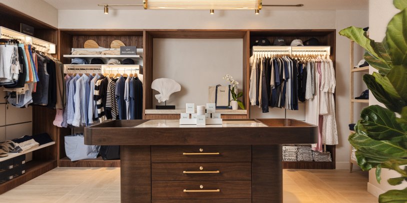 Retail shop with clothing on racks and a brown wood table centered